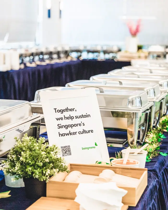 Buffet catering line at a company celebration with a sign about sustaining hawker culture